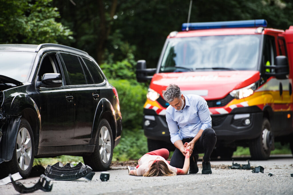 A man helping a young woman lying unconscious on the road after a car accident