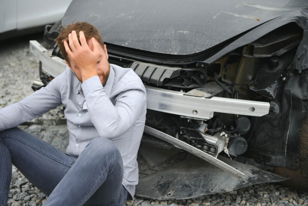 a frustrated man near a broken car grabbing his head